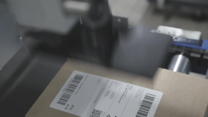 A package being stamped with a shipping label by a machine in a factory