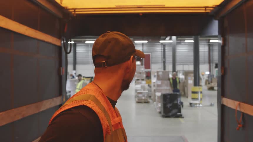 A man has his back turned walking down a bright hallway to a factory