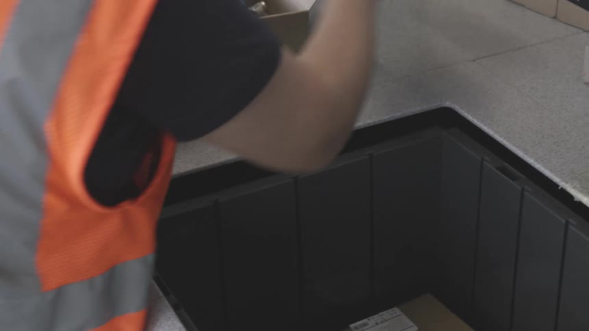 A worker in a safety vest is standing near a table handling cardboard boxes