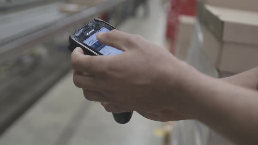 An employee enters info into a device and then grabs a package from a conveyor belt
