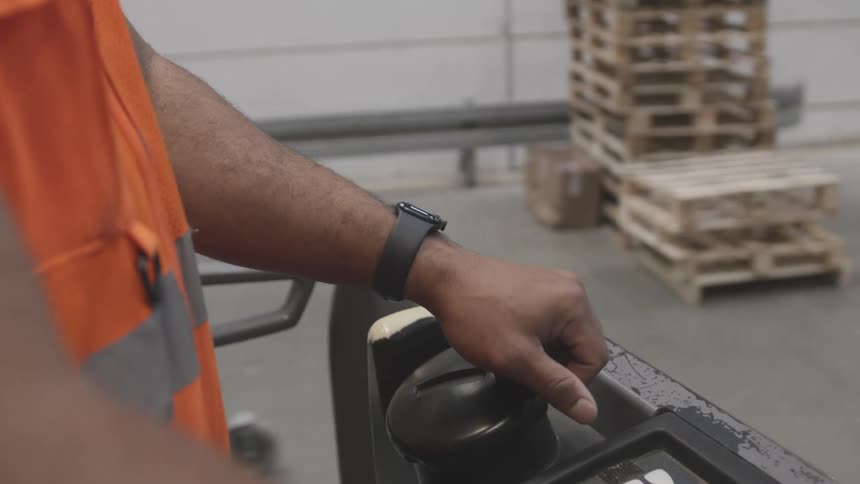 Hand of a man driving a cart inside a logistics center and greeting another group of workers