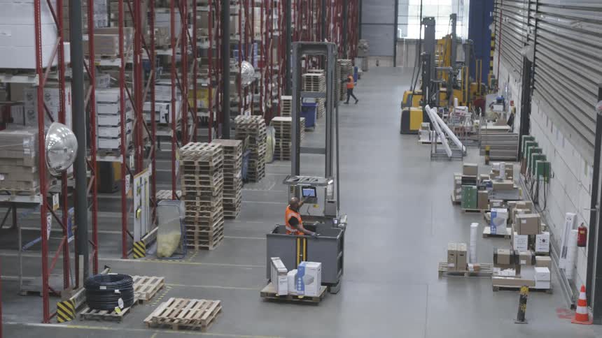 Two men work in a warehouse on a computer and sweeping the floor