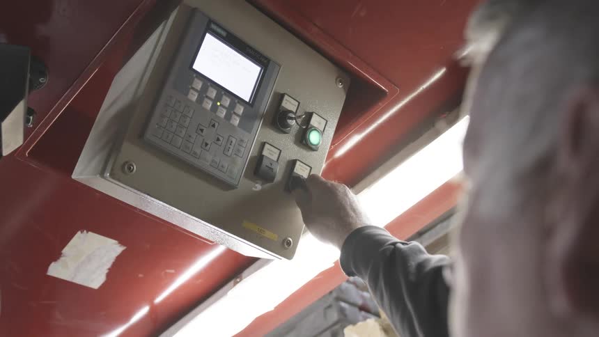 An man operating a control panel on a large red machine with multiple buttons and a display screen