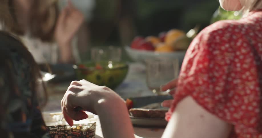A scene of women sitting at a table eating meals while their kids play in the background at the park