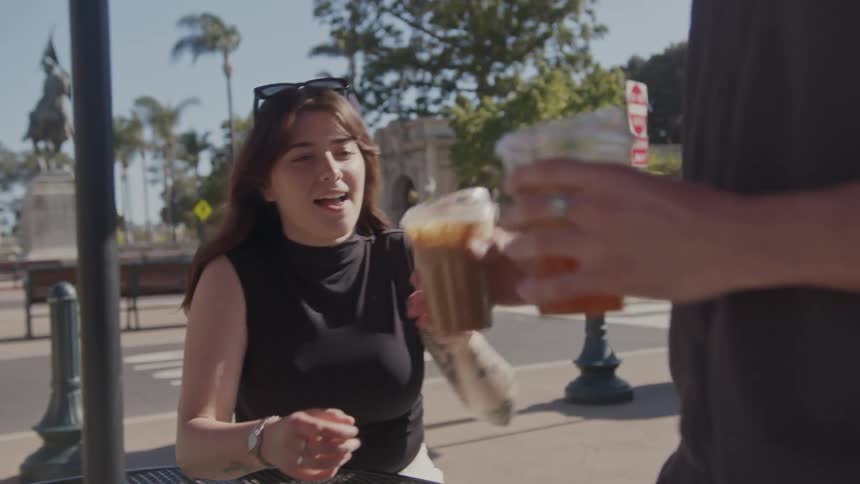 A man brings a drink to a woman on a campus