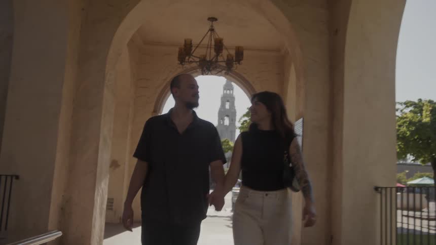 Couple walks hand in hand under covered walkway with landmark tower in the background