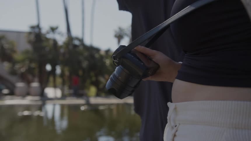 A couple with a camera point while standing near a pond