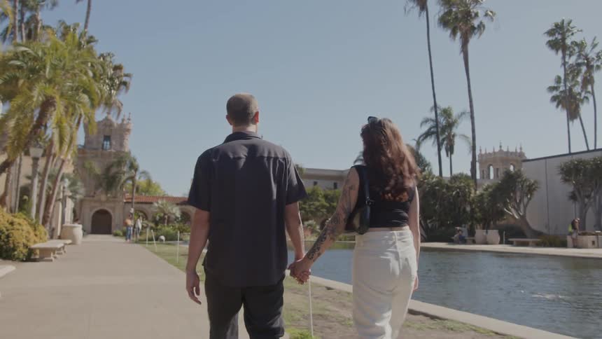 Back view of a couple walking hand in hand beside an artificial lake in a historic square