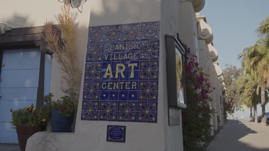 Blue and yellow sign attached to building corner identifies the spanish village art center