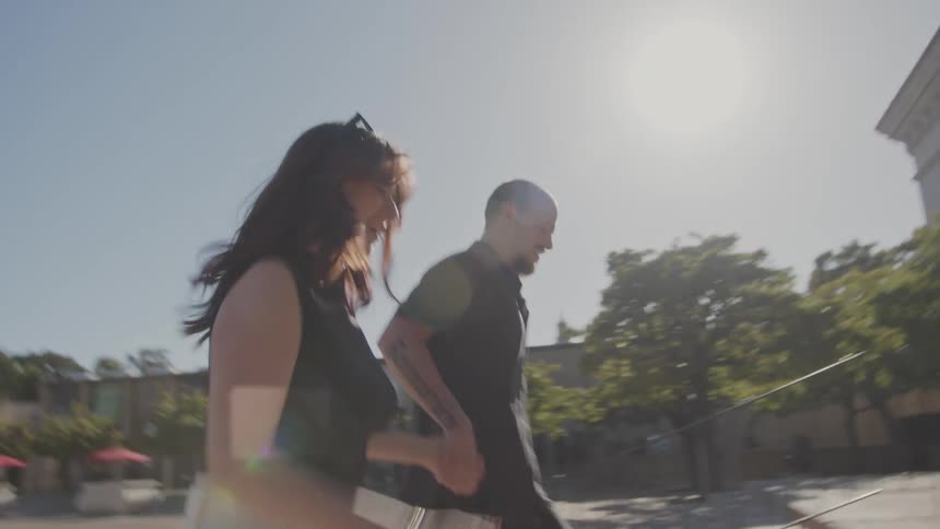 A man in a black outfit and a woman in a black top and white pants walk hand in hand hurrying to enter the san diego museum of art