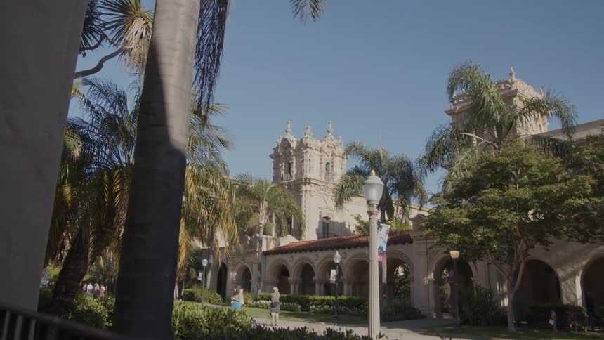 People walk through sidewalk between landmark buildings with towers