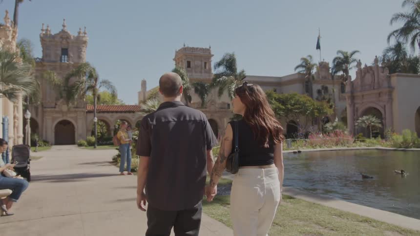A couple walk around a pond near an old building