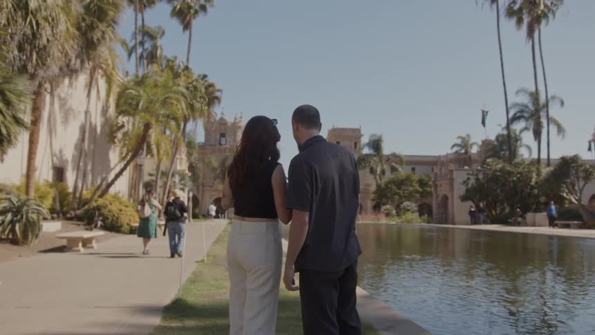 Tourist couple stands near pond taking picture of landmark building