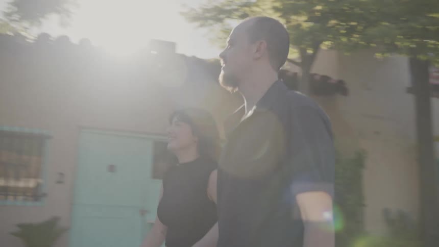 Man and woman walking in a square with houses around them while talking