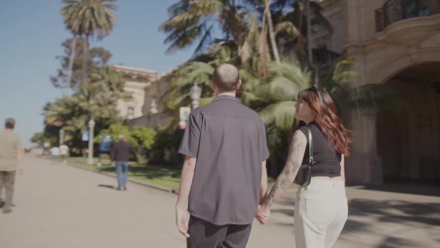 Couple holding hands walk past building with a portico