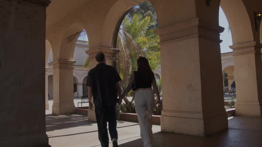 Couple walk hand in hand along an arcade on a sunny day