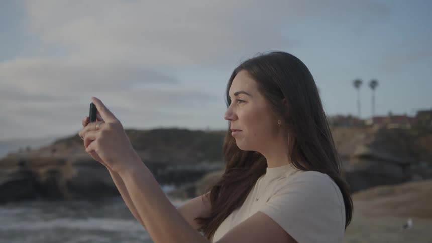 Woman holding a cell phone and taking photos while on a beach