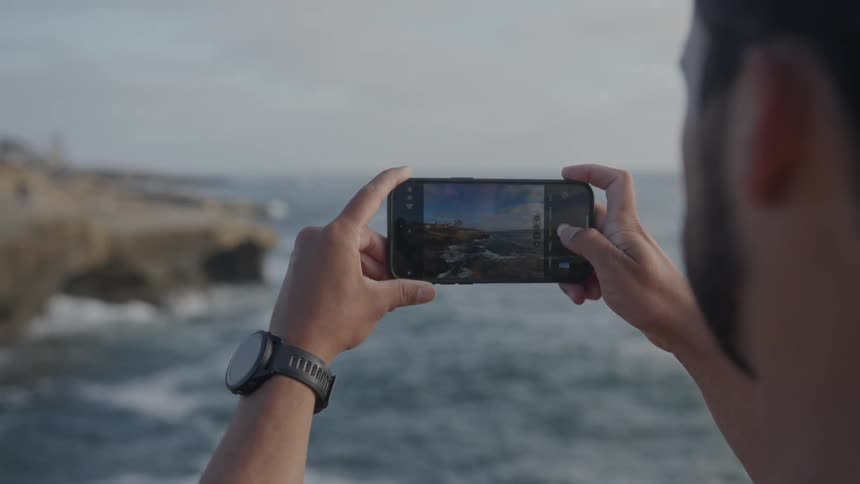 A man uses a smartphone camera to take a picture of a coastal area