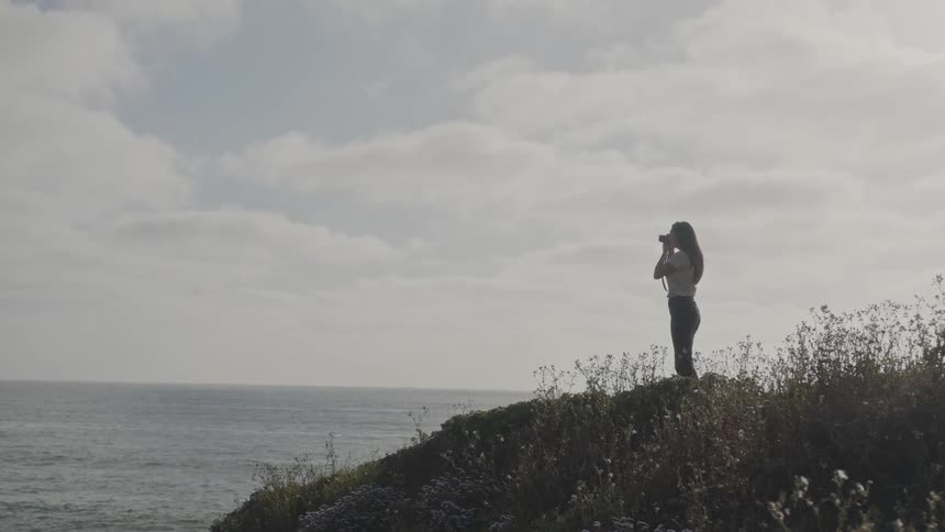 A clip of a lady taking a photograph of the sea