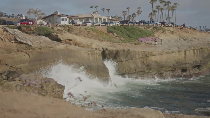 Coastal landscape with waves crashing on rocks and cars parked around