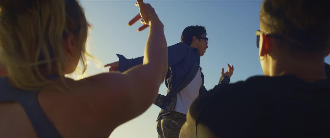 Man standing dancing and two other people sitting enjoying and moving their arms