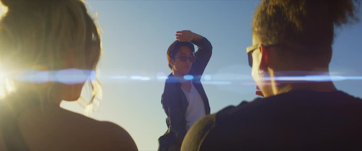 Man and woman sit and watch a third man dance under a glaring sun