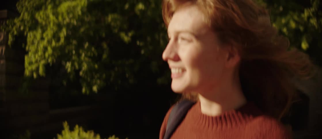 A woman laughs and points while walking near buildings and trees