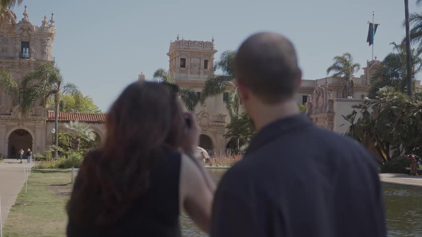 View of a couple from the back and front of a temple with an artificial lake photographing with a camera