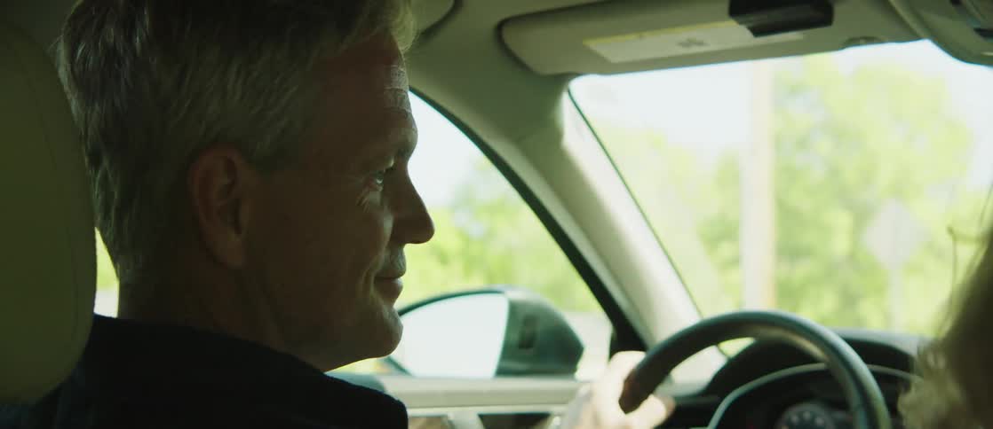 A man drives a car his female passenger and him laugh while talking