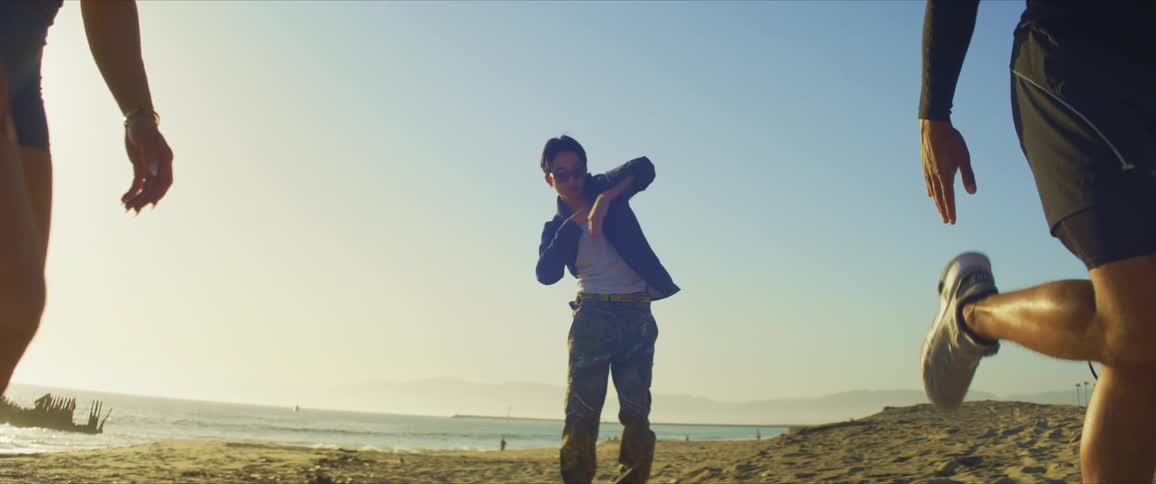 Man dancing on the beach sand while two people beside him stretch their legs