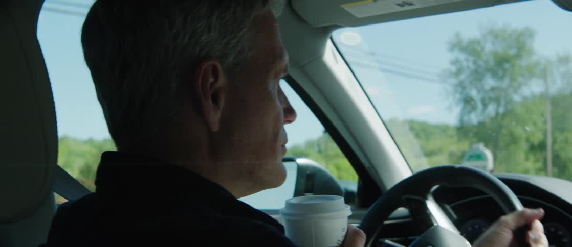Middle aged man wearing a dark shirt drives a car on a highway