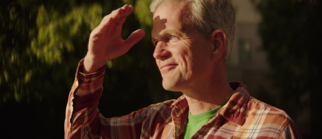 A man stands outdoors shading his eyes from the sun