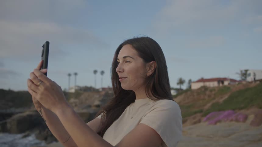 Portrait of a woman using smartphone on the beach and taking videos