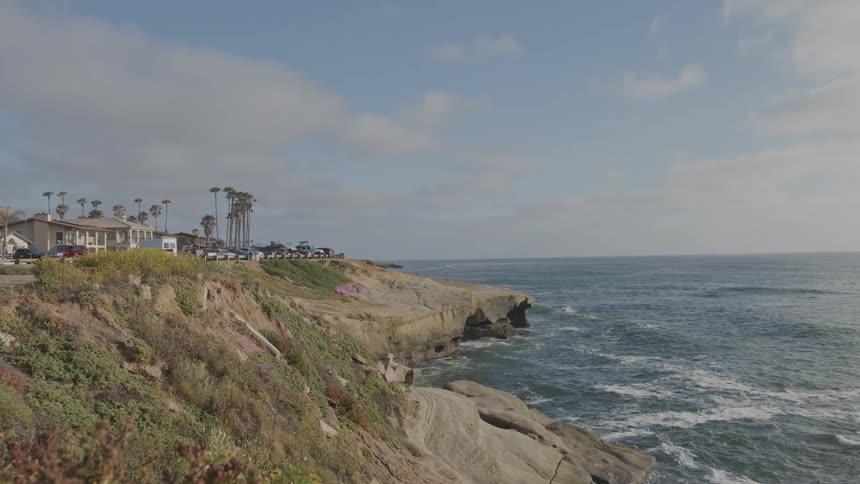 A rugged cliff overlooking an ocean with waterfront buildings in the distance