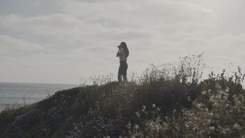 Woman on a hill by the sea taking photos