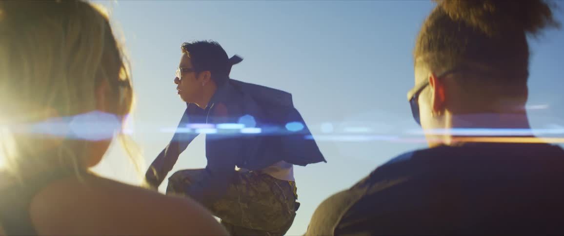 A man and woman both wearing sunglasses and black tops watch a dancer perform with sunlight in the background