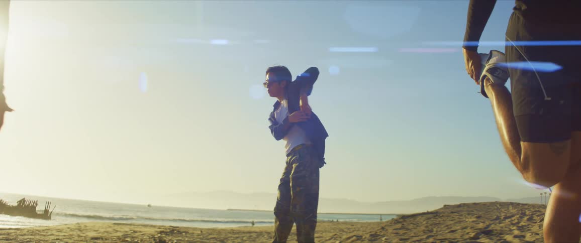 Two people stretching their legs and in the background a man dancing on the beach