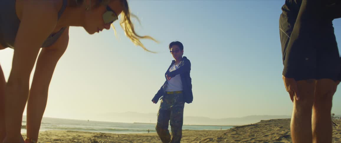 Man with sunglasses dancing on the beach and next to a man and a woman stretching their legs