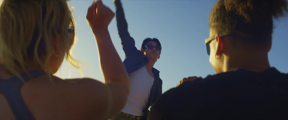 A man and woman both wearing sunglasses and black tops watch a dancer perform with sunlight in the background