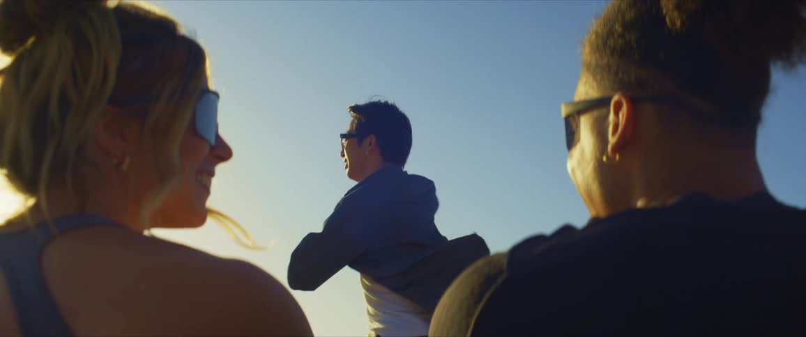 Man with sunglasses and shirt dancing standing up to two spectators who are sitting down enjoying the vibe