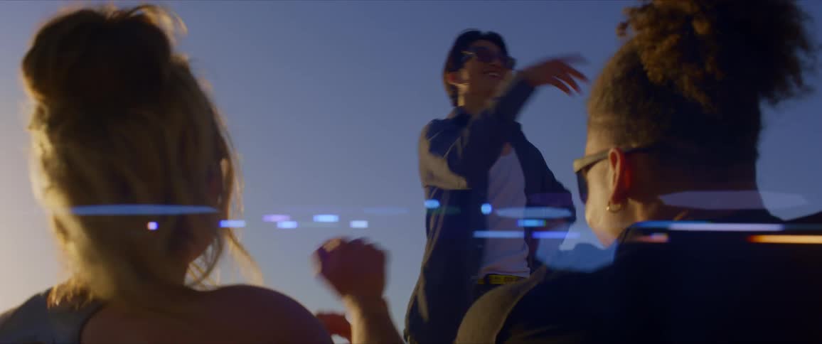 Two women are sitting enjoying themselves as their male friend dances