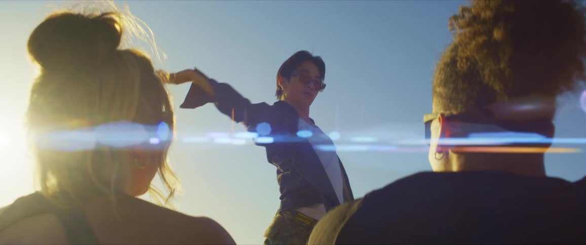 Young man with sunglasses dancing in an openair environment and two people sitting watching him