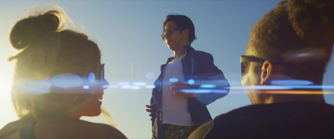 Two friends seen from behind looking at a person dancing with sunlight and a blue sky