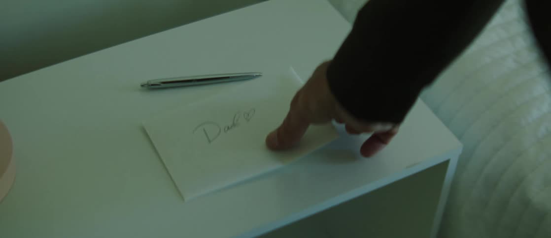 A man wearing a black shirt picks up a letter in the bedroom