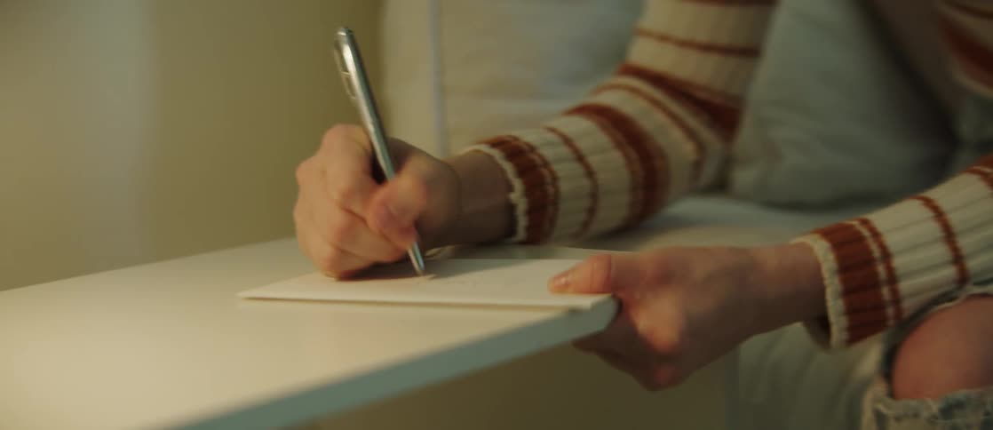 A woman sitting on a bed writes on an envelope