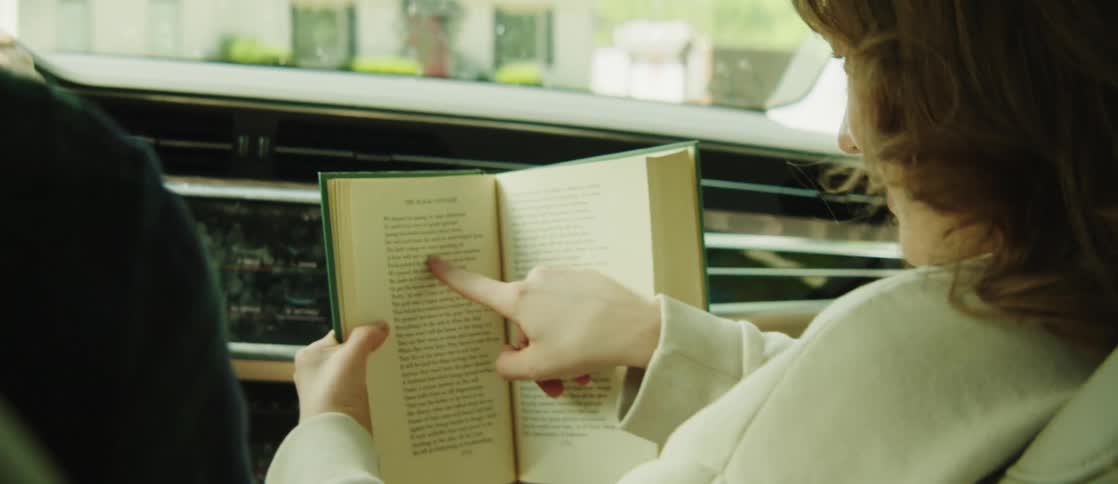 Woman in the front seat of a car reading a book with the help of her index finger