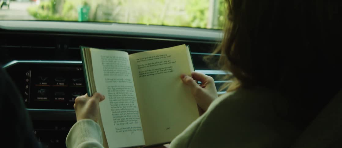A woman is reading a book in the passenger seat of a car