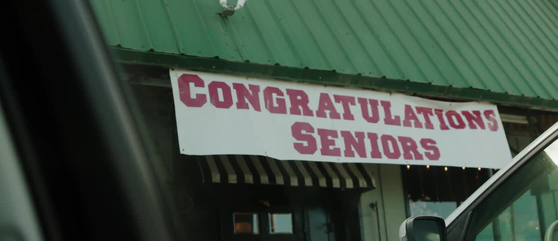 A sign congratulating graduating seniors with congratulations seniors written in large bold letters is seen from a car