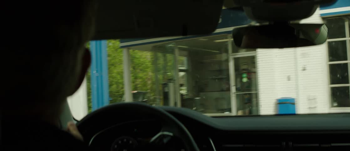 Interior view of a vehicle and a man driving around a curve at a gas station