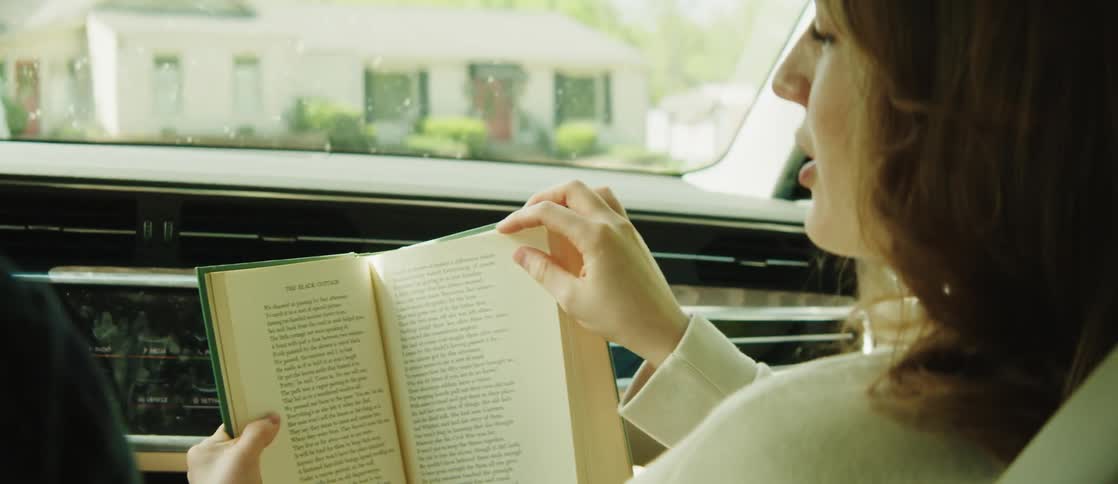 Young woman sitting in the front seat of a moving car reading a book